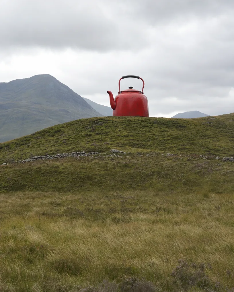 Giant red kettle standing on a green hill under a gray sky