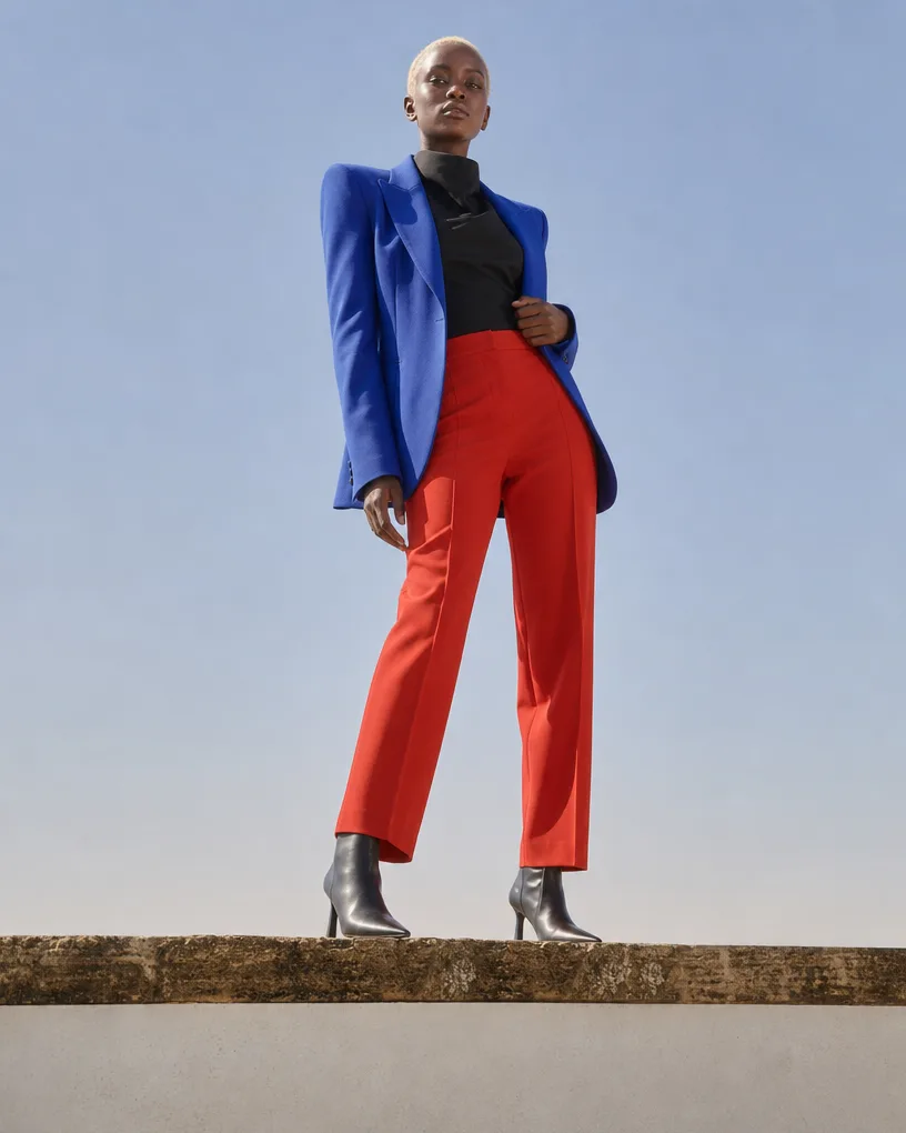 Model in a cobalt blazer and red trousers against open sky