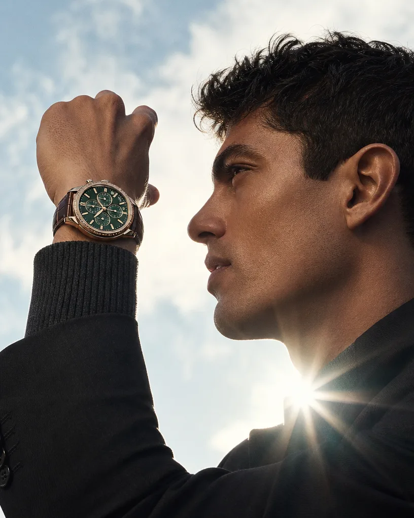Man in profile raising his wrist to the sun, a green-dial chronograph catching the light